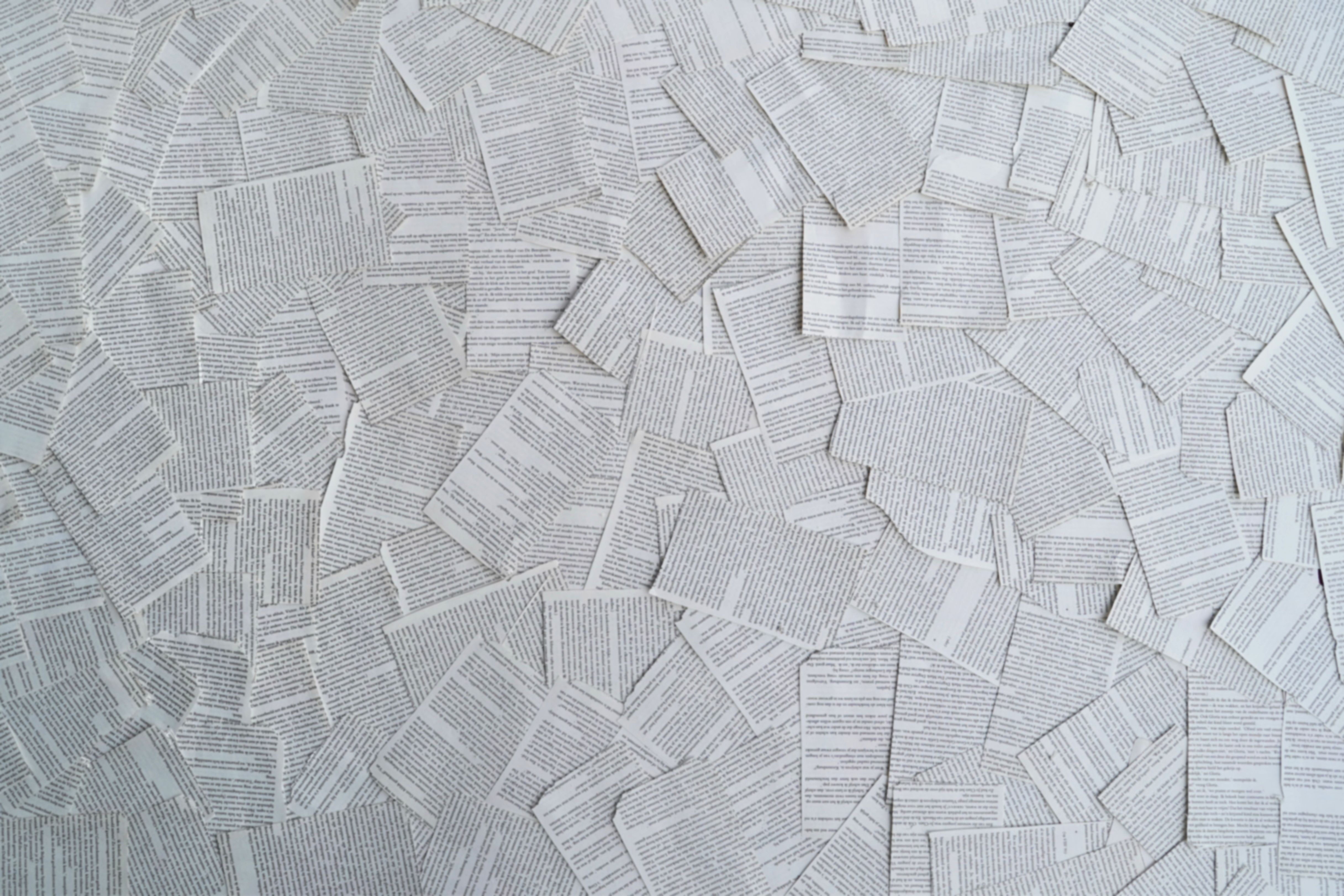 A top view of white and gray text-heavy book pages scattered randomly, creating a textured pattern.