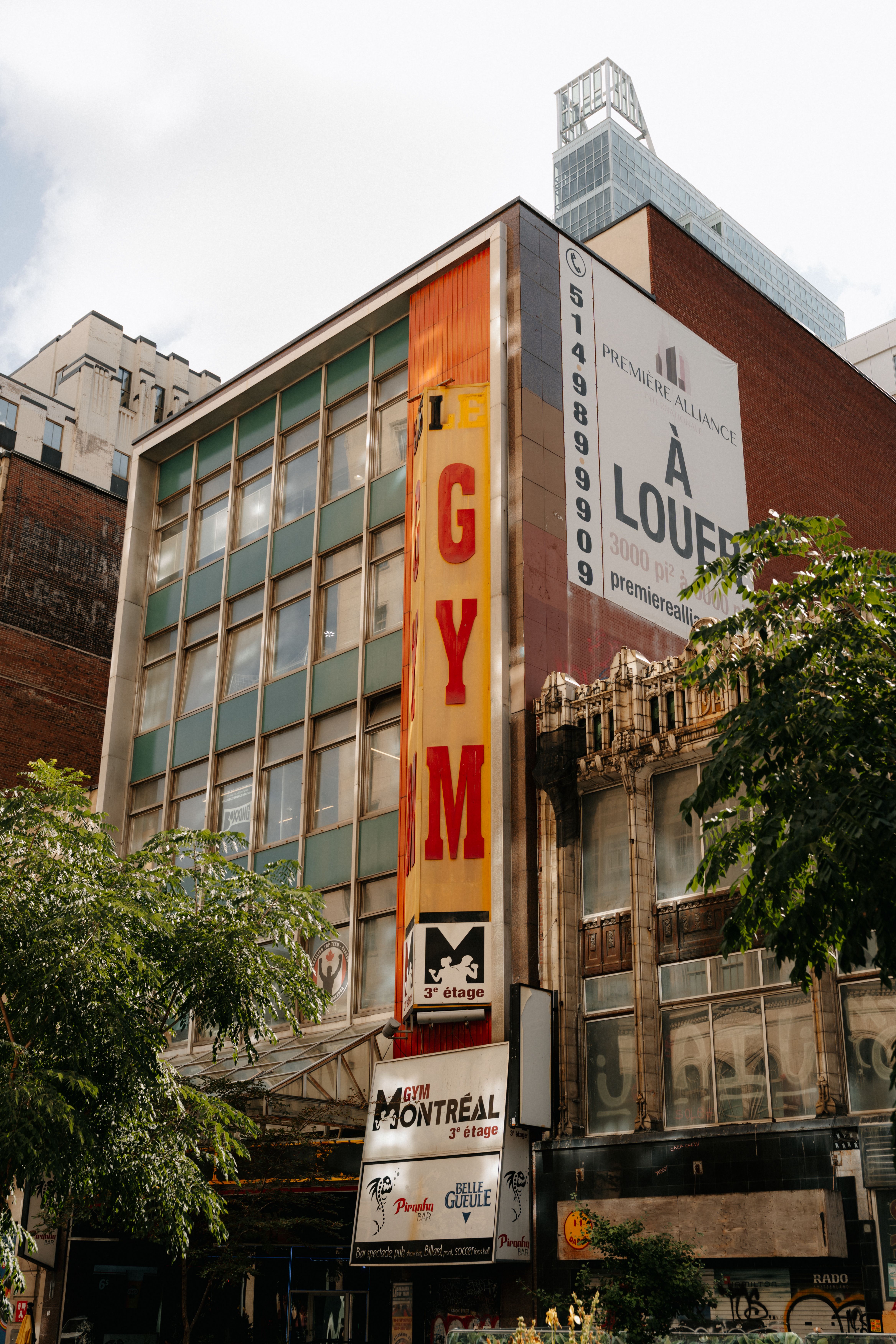 Urban scene in Montréal featuring a building with a prominent gym sign and trees.