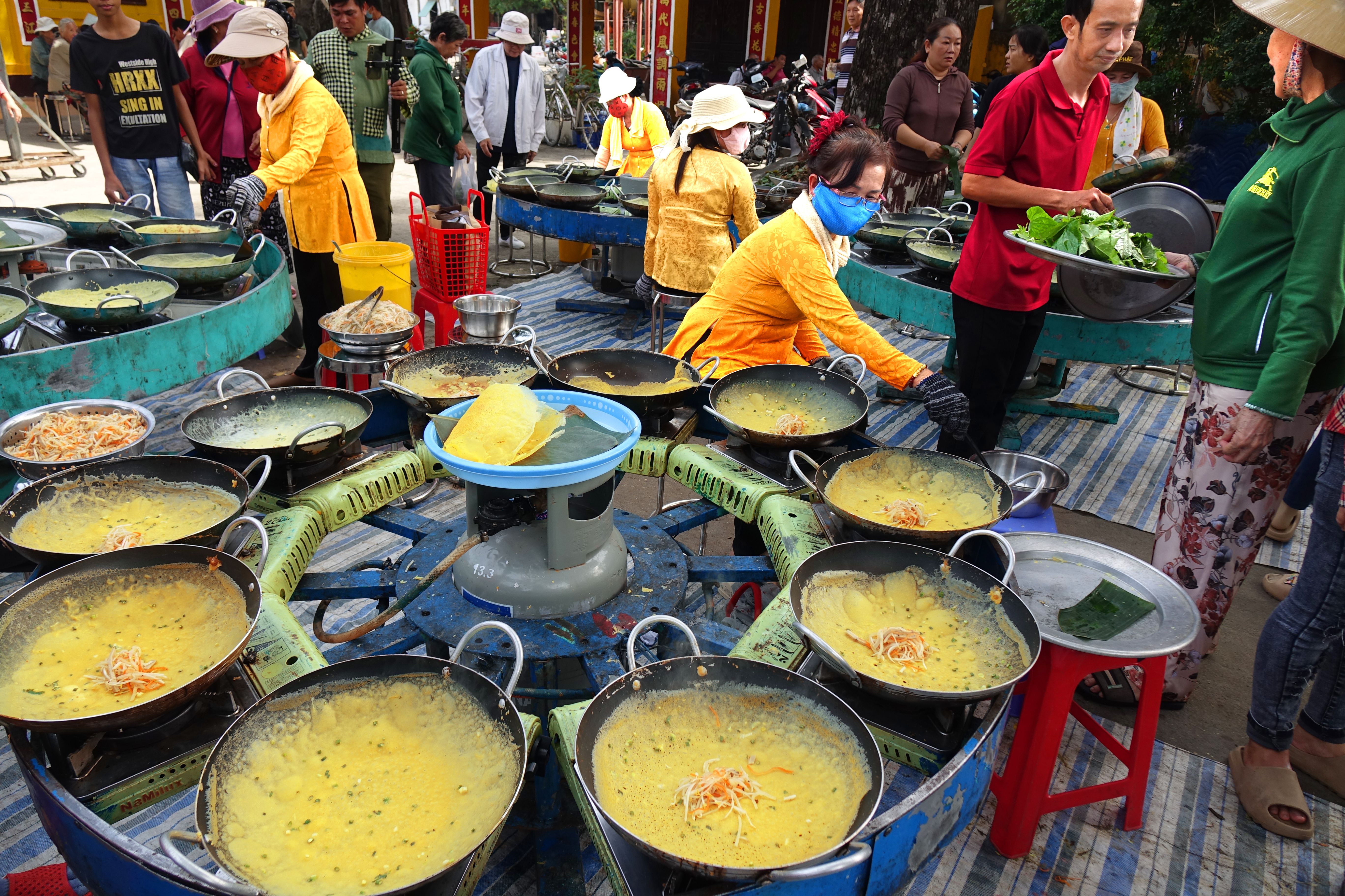 Outdoor street market with multiple food stalls preparing dishes; vibrant and bustling atmosphere.
