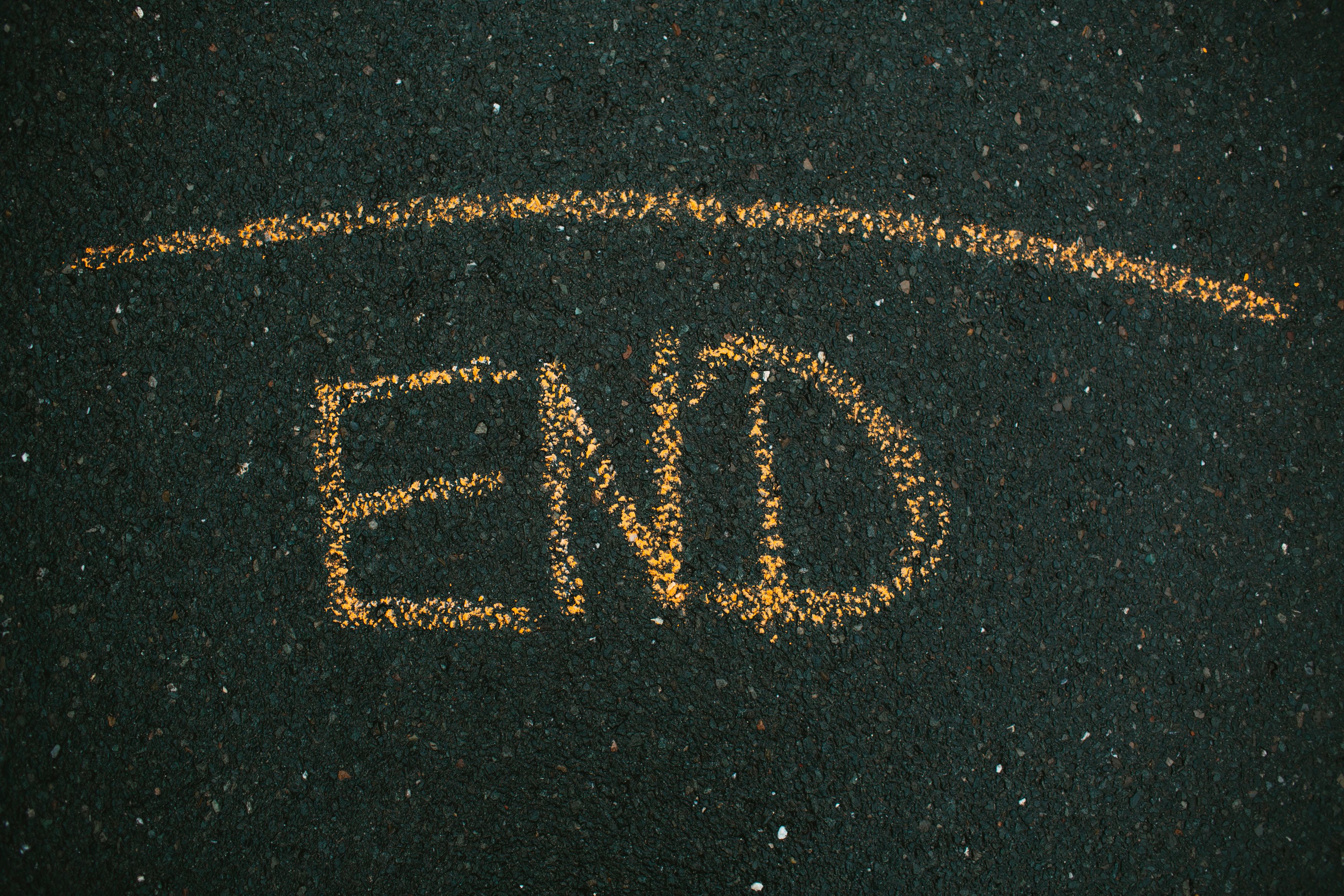 Close-up of 'END' written on asphalt with yellow chalk.