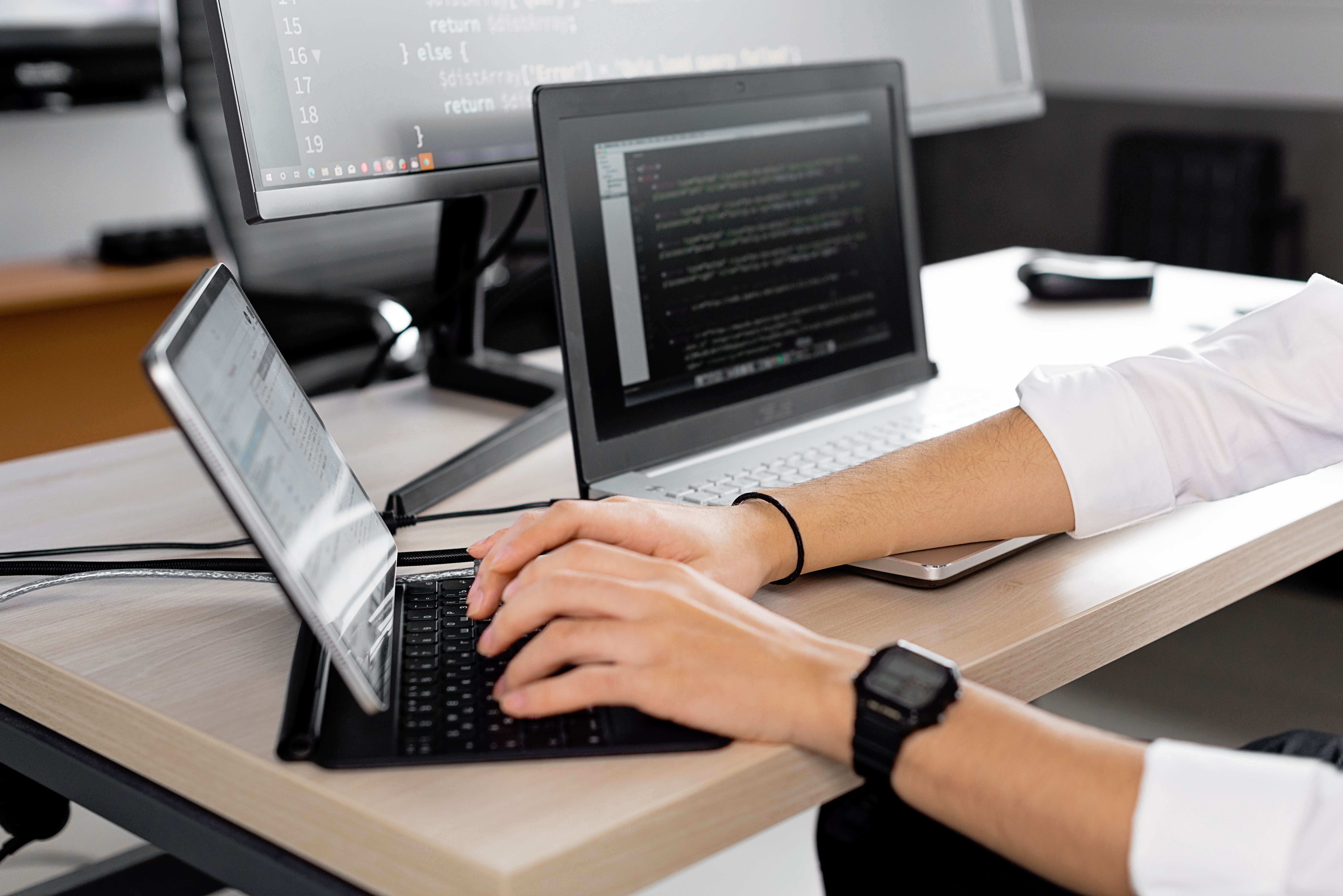 Candid shot of a programmer at work using multiple screens to code in a modern office.