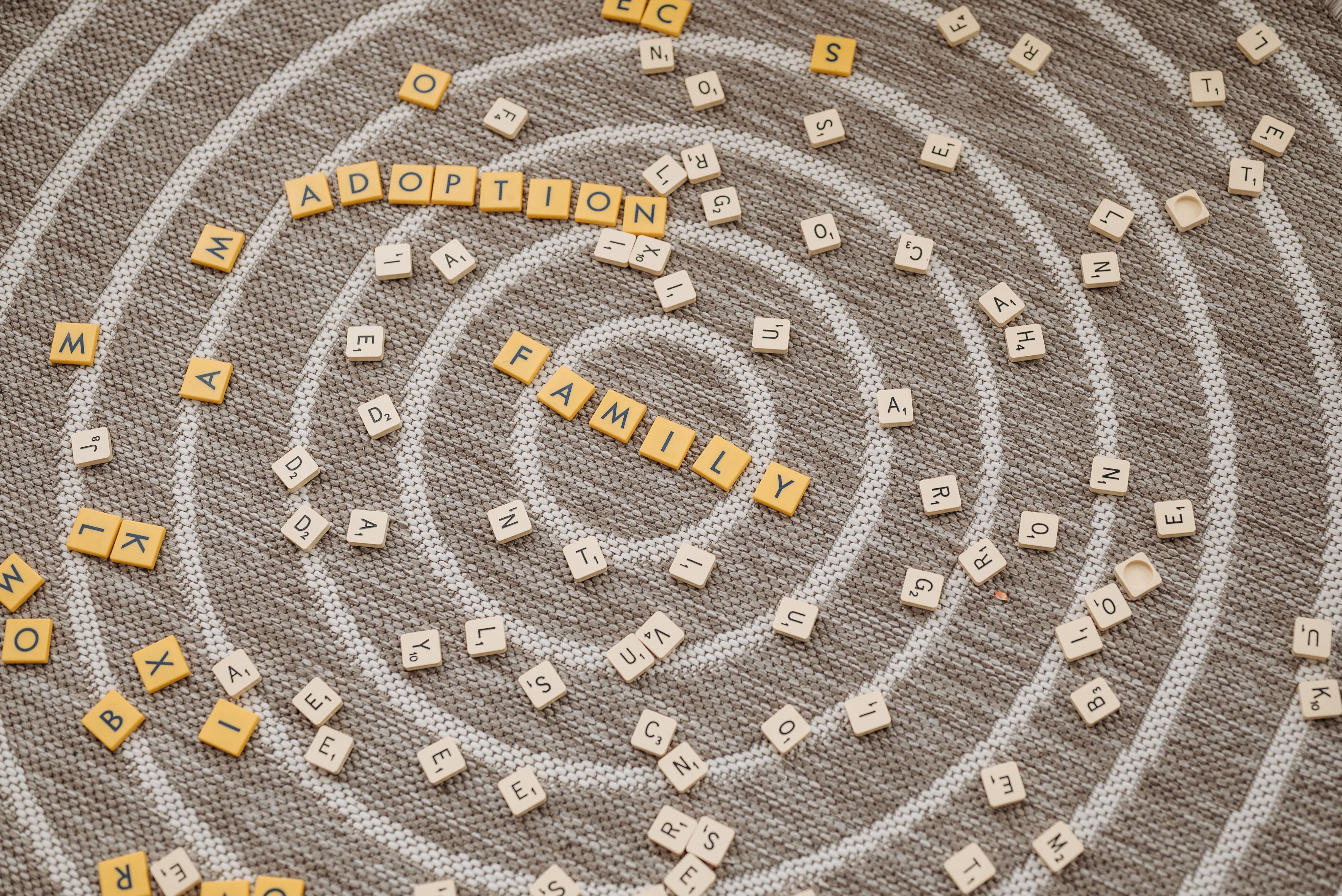 Scrabble tiles spell 'adoption' and 'family' on a textured carpet background, symbolizing family unity.